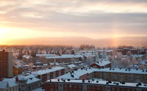 Vintermorgon i Boden, Sverige. Solen går upp över ett snötäckt landskap med hus och träd.