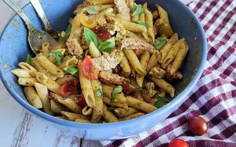 Un plat généreux de penne à la salade pesto, garni de poulet effiloché, tomates cerises et basilic frais. Un délice pour les papilles !