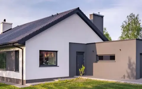 Nowoczesny dom z białymi i szarymi ścianami, ukazujący różne rodzaje elewacji. Dachówka i komin dopełniają całość.