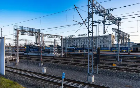 Stacja Gdynia Główna, początek lub koniec najdłuższej trasy kolejowej w Polsce. Tory, perony i budynek dworca pod błękitnym niebem.