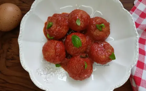 Pallotte cacio e ova in salsa di pomodoro, guarnite con basilico fresco. Un uovo intero è visibile a sinistra.