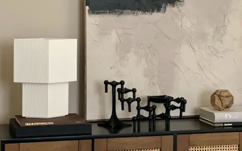 En stilren stilleben inredning med en vit lampa, svarta ljusstakar och en bok med texten "Dior".