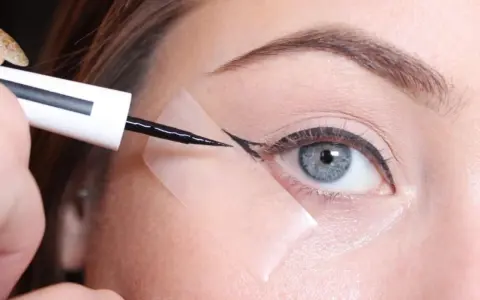 Aplicando delineador con cinta para aprender como hacer la raya del ojo para principiantes. Ojo azul, ceja definida, delineador negro.