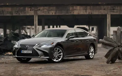 Szary Lexus LS 500h zaparkowany na tle zniszczonej budowli.