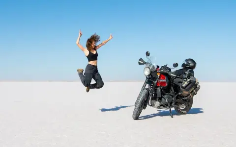 Donna salta di gioia su un deserto di sale, moto pronta per l'avventura. Questo è cosa significa on the road: libertà e scoperta.