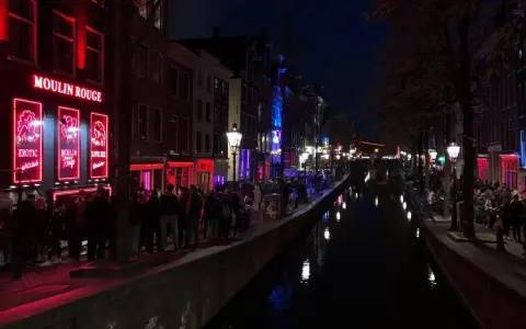 Nocna czerwona ulica Amsterdamu z kanałem i neonami.