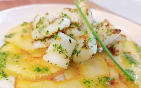 Delicioso plato de sepia al ajillo sobre patatas finas, con perejil picado y un toque de aceite de oliva.