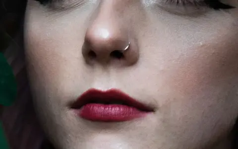 Delikatny kolczyk w nosie, jak rhino piercing, podkreśla pełne, ciemnoczerwone usta.