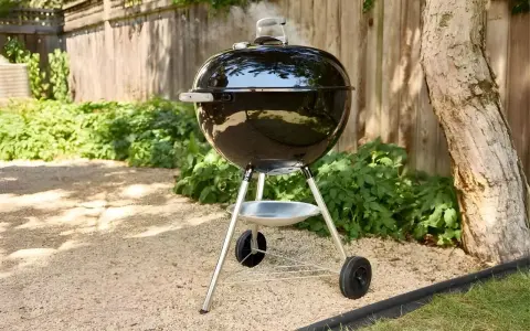 Un barbecue noir fumant, prêt à faire griller de bonnes choses dans le jardin. L'été arrive, il est temps de faire un barbecue !