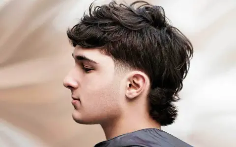 Młody mężczyzna z ciemnymi, kręconymi włosami w nowoczesnej odsłonie fryzury mullet.