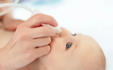 Dłoń podaje krople do noska niemowlaka, by ulżyć mu przy charczeniu.