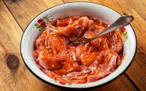 Morceaux de viande crue dans une sauce rouge épicée, prêts à être cuisinés. Une fourchette est plantée dans la préparation.