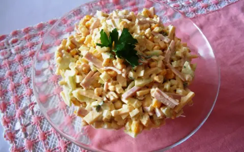 Pyszna sałatka z szynką, kukurydzą i serem, udekorowana natką pietruszki. Idealna na każdą okazję.