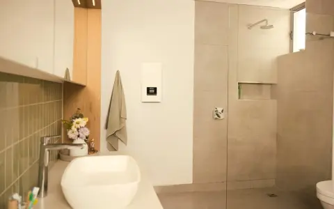 Modernes Bad mit Dusche und Waschbecken. Ein Durchlauferhitzer hängt an der Wand, der für warmes Wasser sorgt, auch wenn man ihn an 230V anschließen möchte.