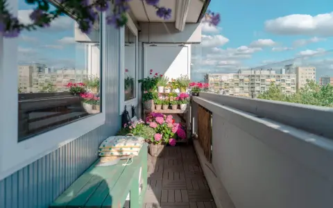 Uroczy balkon z drewnianą podłogą, zieloną ławką i mnóstwem kwiatów. Idealne miejsce, by odpocząć, gdy szukasz pomysłów, co na balkon zamiast płytek.