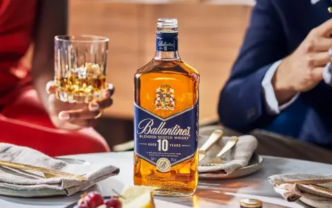 Elegancka butelka Ballantine's 10 Years Old na stole, obok kieliszka z bursztynowym płynem. To nie bourbon, lecz szkocka whisky, idealna na specjalne okazje.