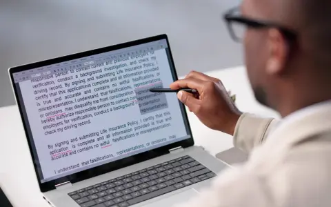 Un homme examine un document sur un écran d'ordinateur, soulignant des passages pour apprendre comment reconnaître une pièce fautée.