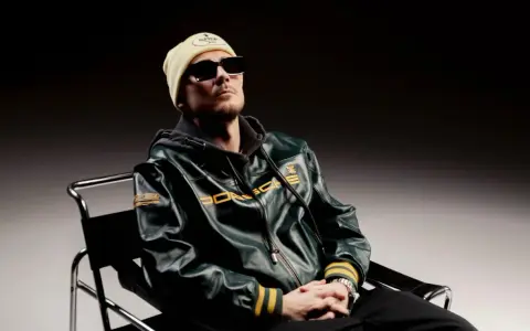 Pezet w skórzanej kurtce Porsche, w bejsbolówce i okularach, siedzi na krześle. Zapowiada nowy album.