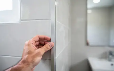 Main tenant vérifie le joint en L d'un profilé de finition sur un mur carrelé.