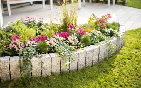 Ein wunderschön bepflanztes Beet mit bunten Blumen und Gräsern, umrandet von Granitsteinen. Perfekt, um neue Ideen für eigene Beet planen zu sammeln.