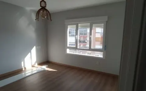 Habitación con suelo de madera, paredes grises y ventana. El sol ilumina la estancia, sugiriendo un buen **precio medio reforma integral**.