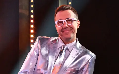 DJ Adamus w srebrnym garniturze i białych okularach, uśmiecha się. Czy to jego odpowiedź na pytanie "Jaka to melodia?