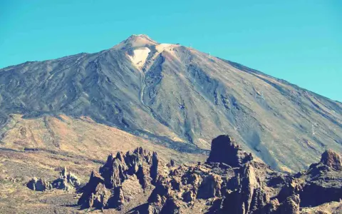 Vulkan Pico del Teide mit felsiger Landschaft im Vordergrund und blauem Himmel.