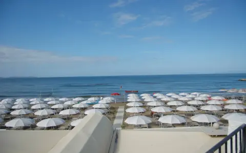 Spiaggia di **Marina di Follonica** con file ordinate di ombrelloni bianchi, mare azzurro e cielo sereno.