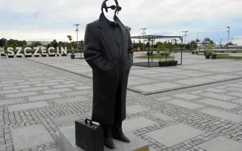 Pomnik Krzysztofa Jarzyny w Szczecinie, z charakterystyczną teczką u stóp, stoi na placu z napisem "SZCZECIN" w tle.