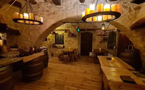 Intérieur d'une taverne médiévale avec murs en pierre, tables en bois et chandeliers. Le tavernier moyen âge y servirait sûrement de l'hydromel.