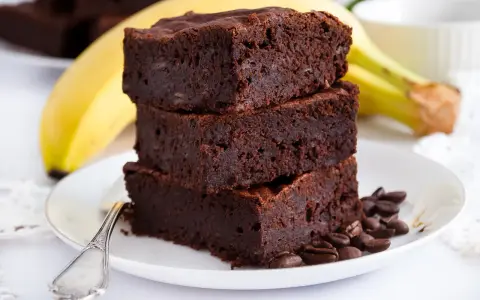Stos puszystych brownie z bananami, ozdobiony ziarnami kawy, na talerzu z bananem w tle.
