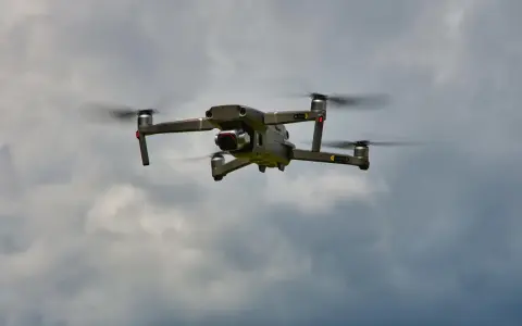 Eine graue Drohne mit roten Lichtern fliegt im bewölkten Himmel. Man kann die Propeller sehen, die sich drehen, während die Drohne in der Luft schwebt. Es ist ein tolles Gefühl, eine Drohne fliegen zu lassen.