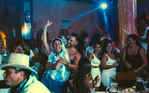 Gente celebrando y bailando en una fiesta, con luces de discoteca y un ambiente festivo. Parece una despedida de soltero con juegos y mucha alegría.