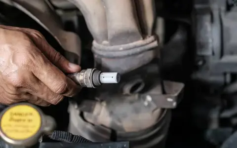Mechanik trzyma w dłoni sondę lambda, przygotowując ją do czyszczenia.