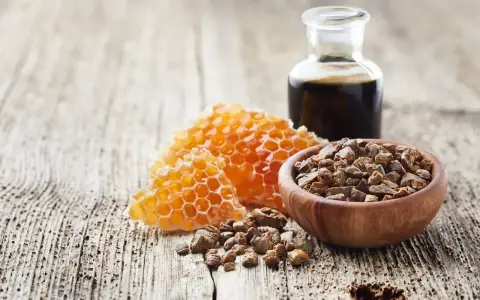 Propolis i pyłek pszczeli w drewnianej miseczce, obok plastra miodu i buteleczki z ciemnym płynem, na drewnianym tle.