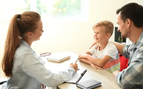 Rodzice rozmawiają z doradcą o tym, jak przenieść dziecko do innej szkoły. Chłopiec uśmiecha się, słuchając rozmowy.
