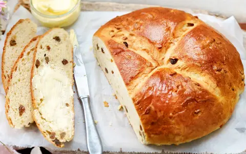 Ein goldbraunes Osterbrot mit Rosinen, aufgeschnitten und mit Butter bestrichen. Perfekt für ein Osterbrot Rezept.
