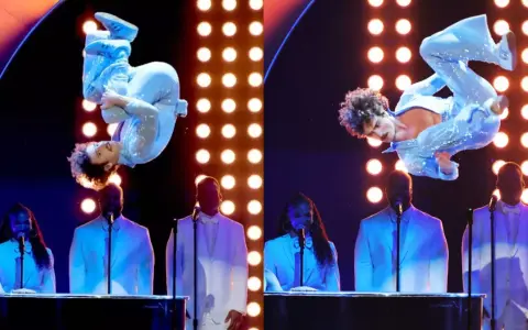 Wokalista w błyszczącym niebieskim stroju wykonuje akrobacje na scenie podczas gali nagród Grammy. Laureaci nagród grammy w białych garniturach stoją za fortepianami.
