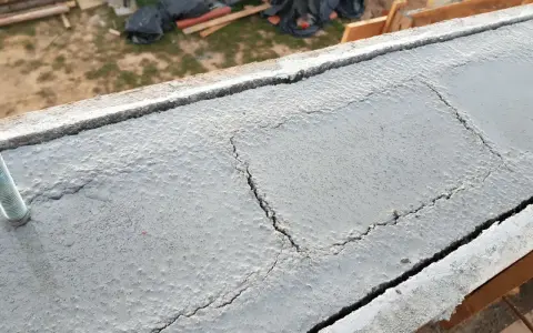 Pęknięty wieniec budowlany z widocznym prętem. Na tle plac budowy.