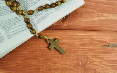 Stary różaniec na drewnianym stole obok Biblii, przypomina o 5 przykazaniach kościelnych.