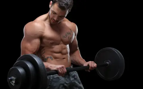 Ein muskulöser Mann mit Tattoos hebt eine Langhantel. Sein Sixpack ist deutlich sichtbar, ein Zeichen für seinen Powerlifting Trainingsplan.
