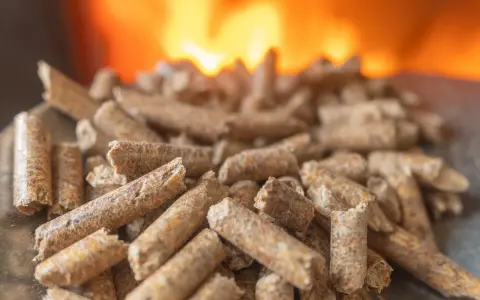 Granulés de bois prêts pour l'installation d'un poêle à granule, avec des flammes chaudes en arrière-plan.