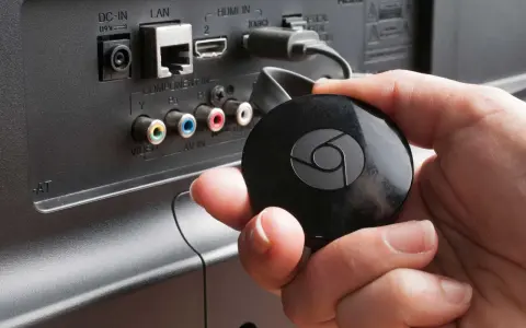 En hand håller en svart Chromecast för att ansluta till en HDMI-port på baksidan av en TV.