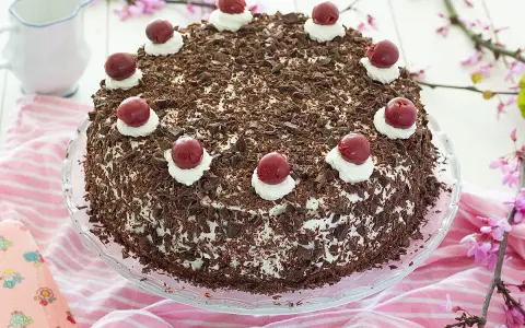 Deliciosa tarta Selva Negra, cubierta de virutas de chocolate y coronada con cerezas y nata.