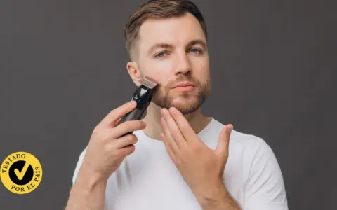 Hombre con barba usando una recortadora para perfilar su rostro. El accesorio "Testado por el país" aparece en la esquina inferior izquierda.