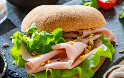 Pyszna włoska kanapka z mortadelą, chrupiącą sałatą i pistacjami na ciemnym tle.