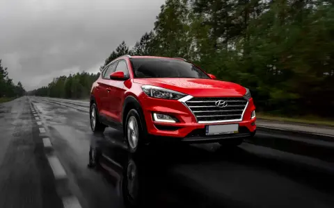 Czerwony Hyundai Tucson jedzie po mokrej drodze w deszczowy dzień. Warto pamiętać o filtrze CPL, którego zastosowanie poprawia widoczność w takich warunkach.