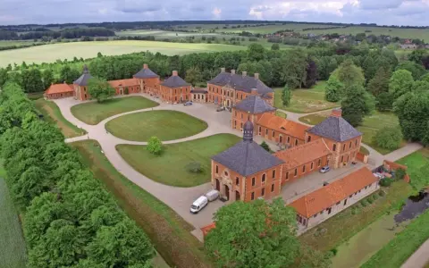 Luftaufnahme von Schloss Bothmer, einem barocken Anwesen mit roten Ziegelgebäuden, umgeben von grünen Gärten und Feldern.