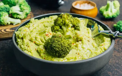 Un bol de purée de brocolis onctueuse, garni de fleurettes de brocolis et d'épices rouges. Un délice vert et sain.