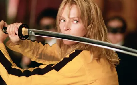 La Novia, con su icónico traje amarillo, desenvaina su katana. La banda sonora de Kill Bill resuena en esta escena de acción.